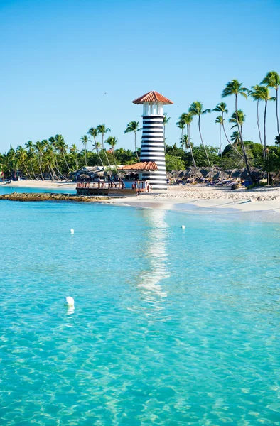 Faro a rayas en la orilla arenosa con palmeras. Agua clara del mar Caribe . — Foto de Stock