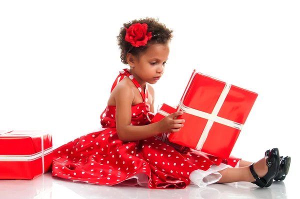 Curly girl in a red polka-dot dress parses New Year holiday gifts — Stockfoto