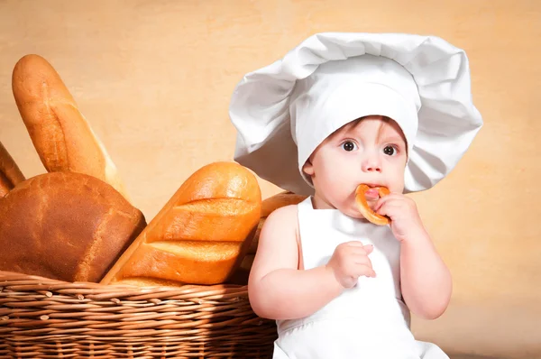 Pequena cozinheira com um bagel nas mãos . — Fotografia de Stock