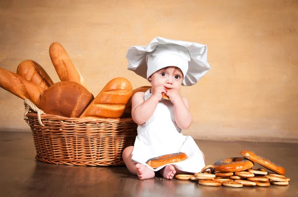 Pequena cozinheira com um bagel nas mãos . — Fotografia de Stock