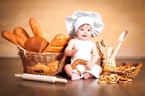 Pequena cozinheira com um bagel nas mãos . — Fotografia de Stock