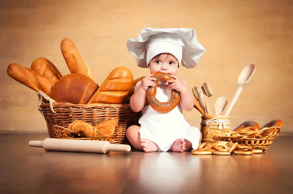 Pequena cozinheira com um bagel nas mãos . — Fotografia de Stock