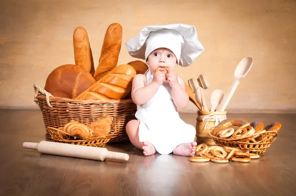 Pequena cozinheira com um bagel nas mãos . — Fotografia de Stock