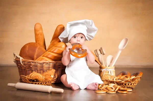 Pequena cozinheira com um bagel nas mãos . — Fotografia de Stock