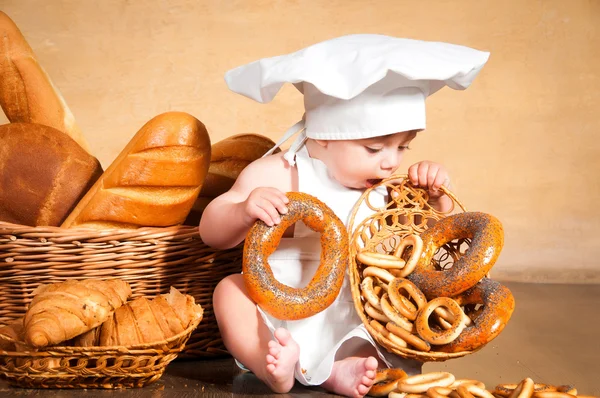 Kleine Köchin mit einem Bagel in der Hand. — Stockfoto