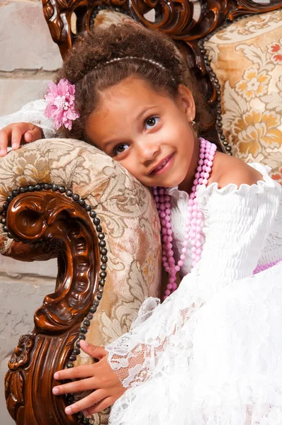 Chica africana sonriente con el pelo rizado en un vestido de encaje blanco en la silla vintage —  Fotos de Stock