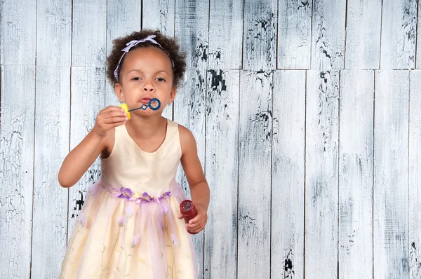 Happy smiling african  girl blowing soap bubbles on the background of wooden wall — Stock Photo, Image