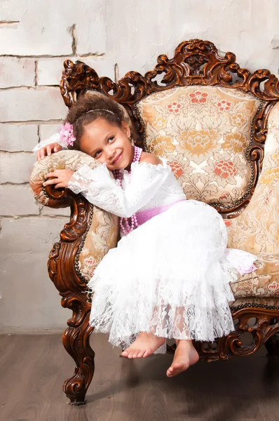 Närbild porträtt leende afrikansk flicka i en vit spetsklänning på vintage stol — Stockfoto