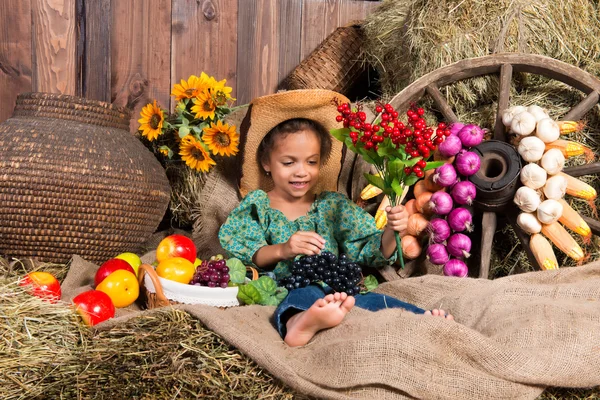Menina africana em chapéu de cowboy sentado no saco de palha com frutas — Fotografia de Stock