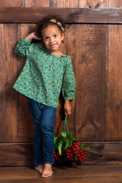 Sonriente niña africana en camisa rural con racimo de bayas sobre fondo de pared de madera marrón — Foto de Stock