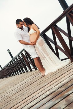 Mutlu hamile çift ahşap köprü üzerinde deniz kıyısında Beyaz giysili