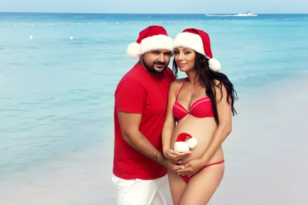 Happy pregnancy, pregnant family. Expectant parents in Christmas costumes and Santa hat on the sea.