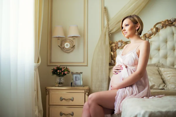 Счастливая беременная девушка сидит в интерьере с роскошной итальянской мебелью и обнимает животик — стоковое фото