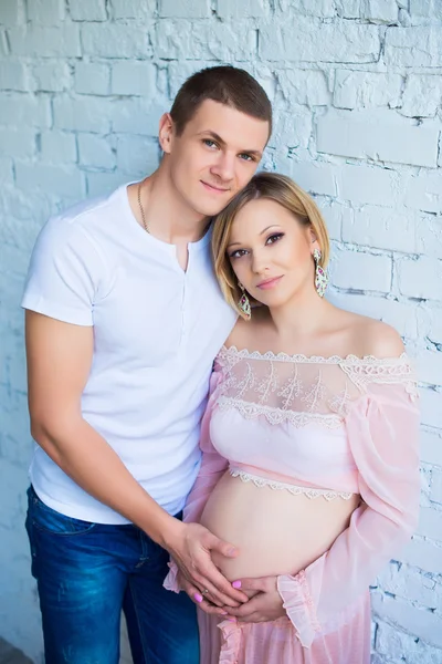 Marido e mulher grávida perto da parede de tijolo branco . — Fotografia de Stock