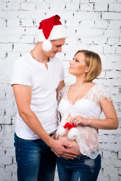 Genç hamile çift küçük çocuk Noel Baba şapkası ile beyaz duvara yakın: — Stok fotoğraf