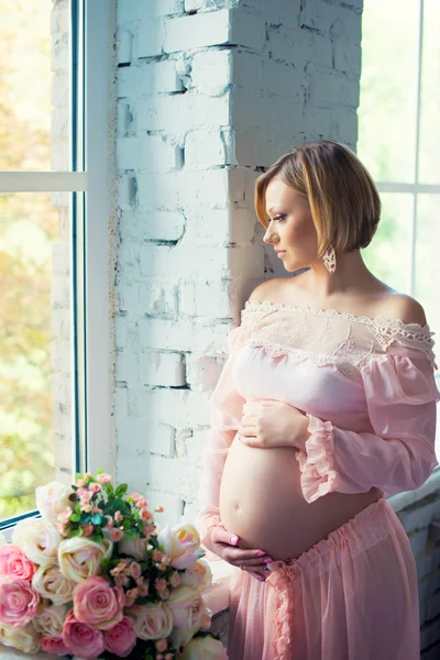 Schwangere Mädchen in der Nähe des Fensters umarmen Bauch. glückliche 9 Monate Schwangerschaft und wartendes Baby — Stockfoto