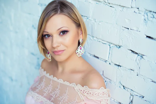 Portrait of pretty young blond woman with short hair on a background of white brick wall — Stock Photo, Image