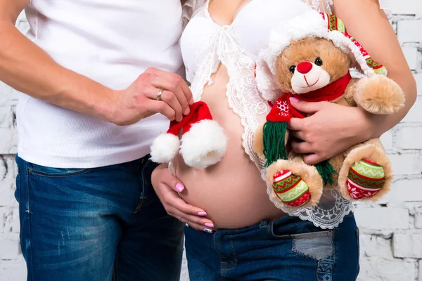 Close-up de barriga grávida, chapéu de Ano Novo de Papai Noel e urso de pelúcia de Natal . — Fotografia de Stock