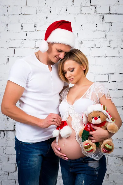Young pregnant family with a New Year Santa hat and Christmas teddy bear. Happy pregnancy