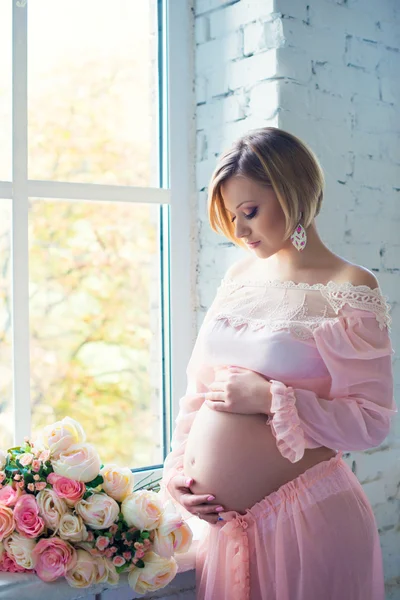 Schwangere Mädchen in der Nähe des Fensters umarmen Bauch. glückliche 9 Monate Schwangerschaft und wartendes Baby — Stockfoto
