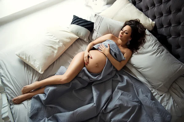 İnce yapılı esmer hamile kadın üzerinde güzel bir yatak çarşafları yalan.
