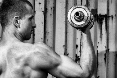 Agray metal duvar arka planı ağır dumbbell ile egzersiz yapan genç atletik erkek kadar kapatın