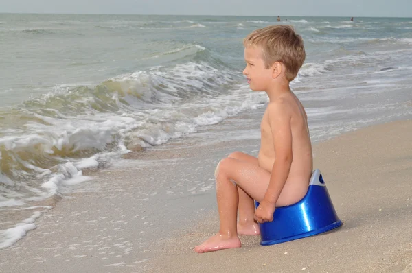 Ragazzo seduto su un vasino sulla riva del mare — Foto Stock