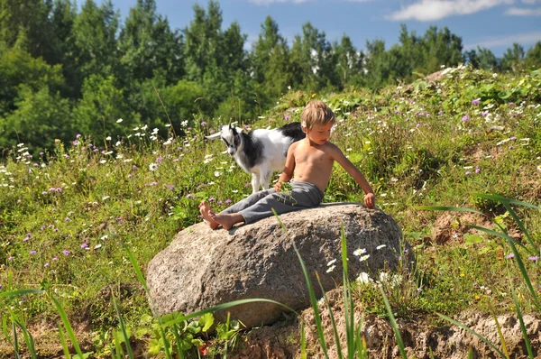 Jongen en geit spelen op een steen — Stockfoto