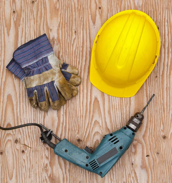 Hard hat, gloves and power drill on wood. Top down view.