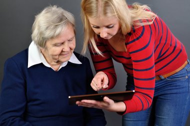 Young woman learns older woman how to use tablet. clipart