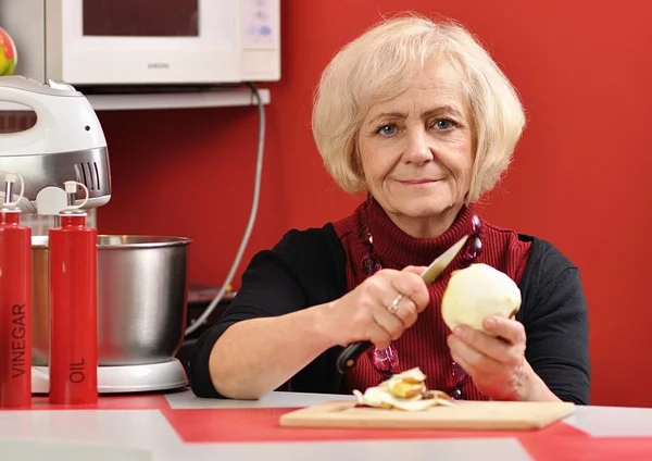 Mature woman peeling apple in the red kitchen. — Stock Photo, Image