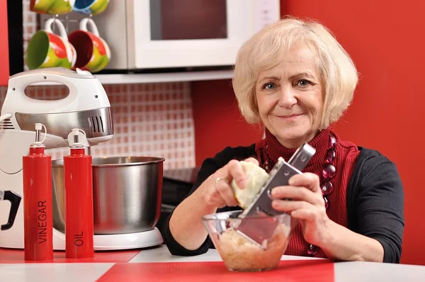 Зрелая женщина готовит очищающее яблоко на красной кухне . — стоковое фото