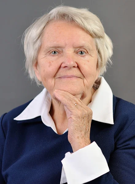 Senior gelukkig vrouw met grijze haren tegen de grijze achtergrond. — Stockfoto