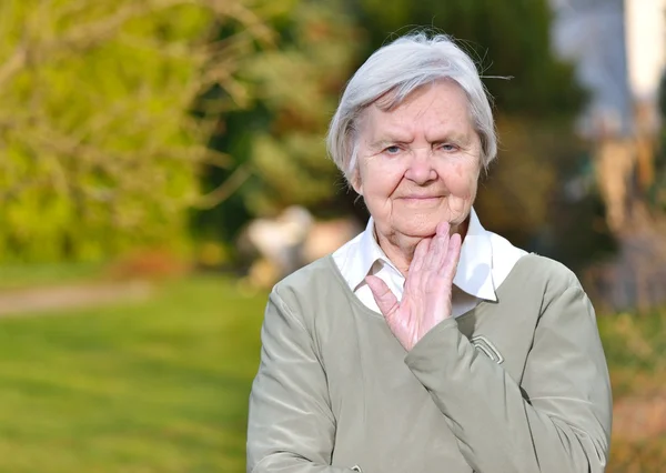 Äldre kvinna ler och drömmer i trädgården. — Stockfoto