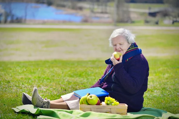 Senior woman eating apple in the park — Stok fotoğraf