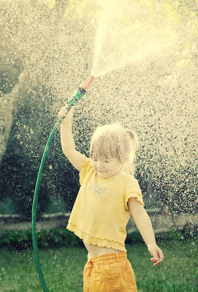 Girl playing in the garden with hose — Stockfoto