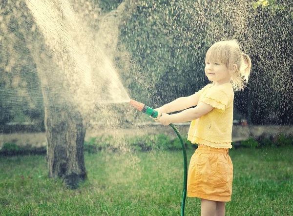 Ragazza che gioca in giardino con il tubo — Foto Stock