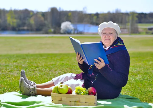 Senior kvinna läser en bok i parken Royaltyfria Stockbilder