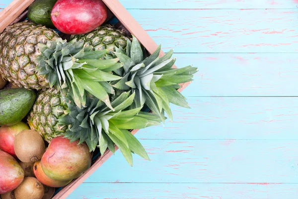 Caja de frutas tropicales en caja sobre mesa azul —  Fotos de Stock