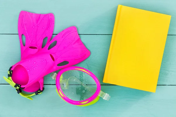 Bright flippers, goggles and book on a green table — Stock Photo, Image