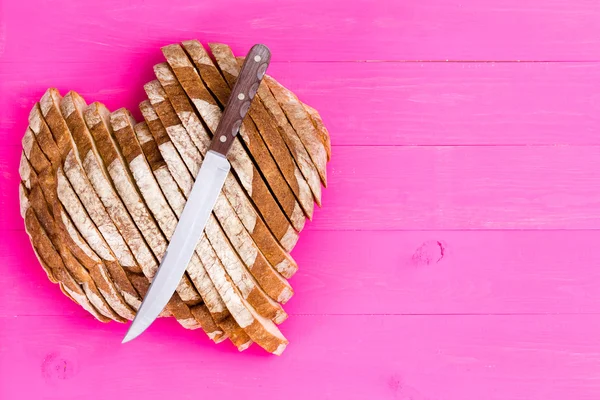 Heart shaped bread and knife on pink background — Stock Photo, Image