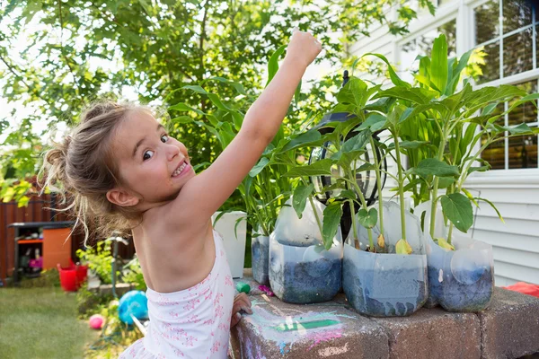 Liten flicka plantera blommor i plastflaskor — Stockfoto