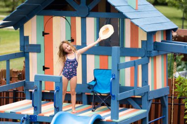 Celebrating child waving hat on outdoor playset clipart