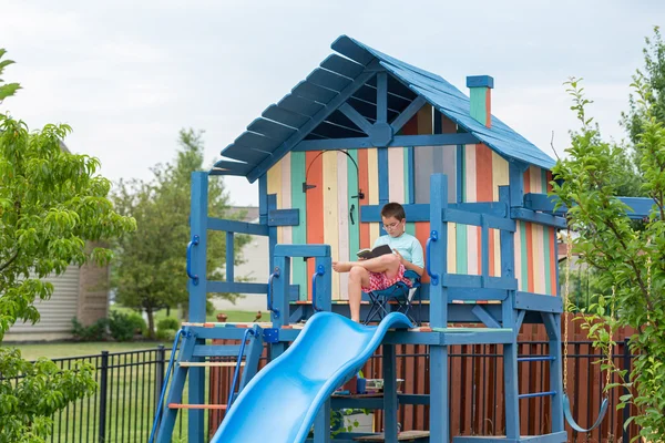 Boy on chair reading while seated on playhouse — Stock Photo, Image