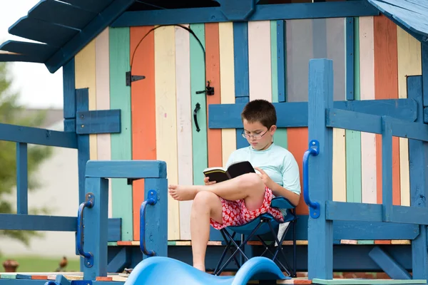 Young boy sitting reading on a wooden playground — Stock Photo, Image