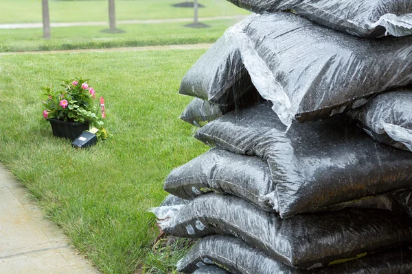 Gestapelde plastic zakken van mulch en bloemen in de regen — Stockfoto