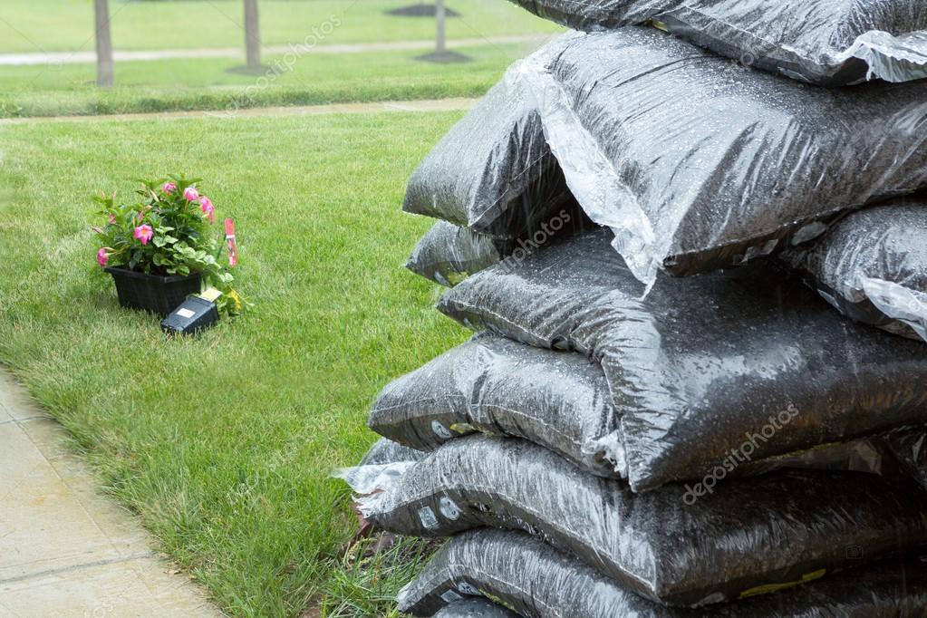 Stacked plastic bags of mulch and flowers in rain Stock Photo by