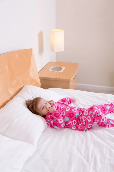 Kleines Mädchen im rosafarbenen Schlafanzug auf einem Bett liegend — Stockfoto