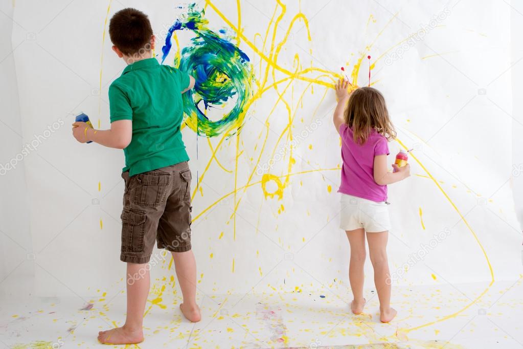 Two young children freehand painting on a wall