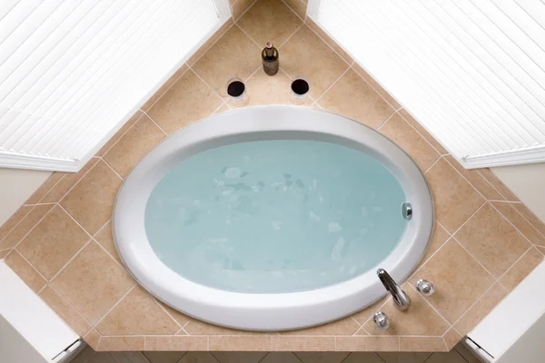 Стильная угловая овальная ванна в окружении плитки — стоковое фото